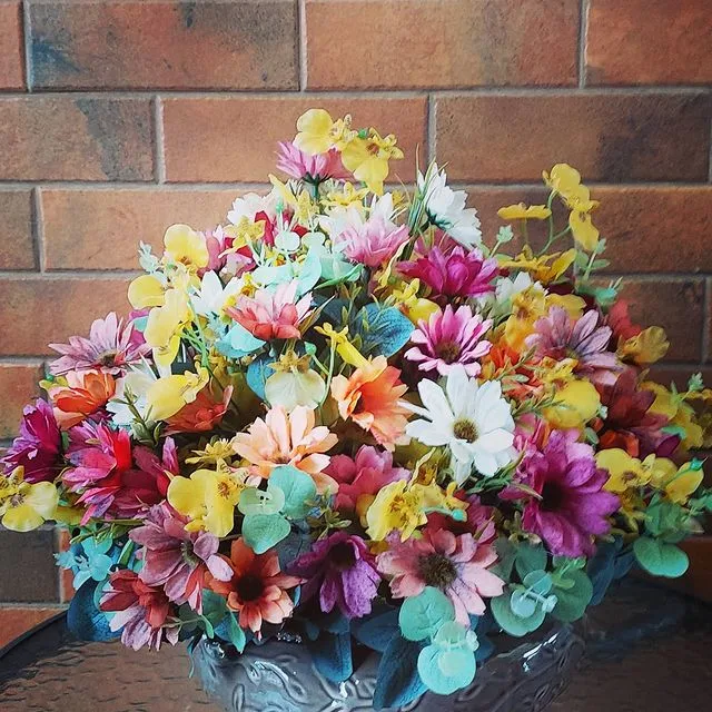 Arranjo de flores coloridas sobre mesa, com parede de tijolos ao fundo